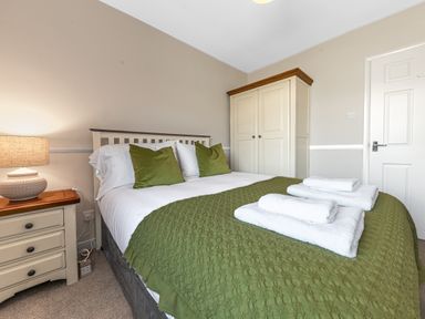 A bedroom with a double bed green pillows and throw towel stacks on the bed beside a nightstand with a lamp and a white wardrobe at Colt Park Cottage in Ulverston
