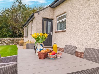 An outdoor table with yellow flowers croissants fruit and orange juice near a house with a black door and windows at Colt Park Cottage in Ulverston