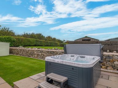 An outdoor hot tub with steps on a patio next to a lawn and a stone wall at Colt Park Cottage in Ulverston