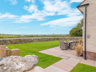 A garden with green grass stone wall and outdoor dining table with chairs at Colt Park Cottage in Ulverston