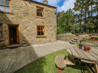 A stone cottage with a wooden door and windows a curved wooden picnic table with plants and a bottle on it in the garden at Moorgair Cottage Slaley near Hexham