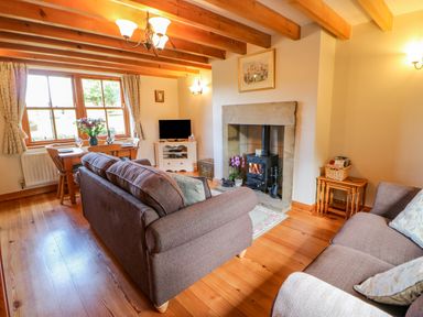 A living room with wooden beams a dining table a fireplace and two sofas at Moorgair Cottage Slaley near Hexham
