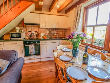 A kitchen with wooden dining table set with plates and wine glasses flowers in a vase and a bottle near a window at Moorgair Cottage Slaley near Hexham