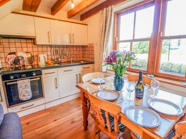 A kitchen with dining table set with plates glasses flowers and a bottle at Moorgair Cottage Slaley near Hexham