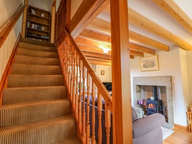 A wooden staircase with carpet leading up next to a living room with a fireplace and wooden ceiling beams at Moorgair Cottage in Slaley near Hexham