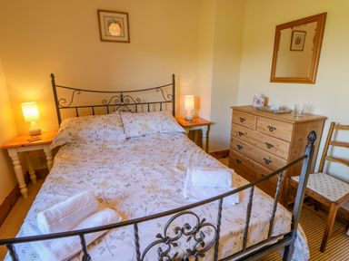 A bedroom with a double bed bedside tables lamps a wooden dresser a mirror and a wooden chair at Moorgair Cottage in Slaley near Hexham