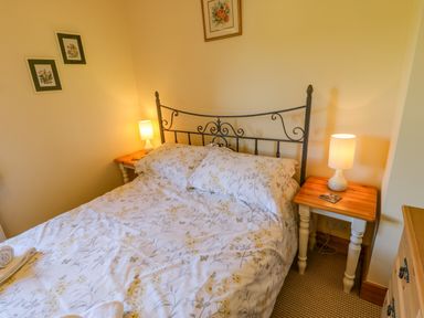 A bedroom with a floral bedspread on a bed with a metal headboard and two wooden bedside tables with lamps at Moorgair Cottage Slaley near Hexham