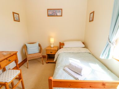 A small bedroom with a single bed with folded towels bedside table lamp wicker chair and wooden desk at Moorgair Cottage Slaley near Hexham