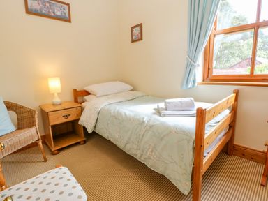 A bedroom with a single bed a bedside table with lamp a chair and a window with curtains at Moorgair Cottage in Slaley near Hexham