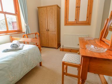 A bedroom with a bed with folded towels a wooden wardrobe a dressing table with a stool and a window at Moorgair Cottage in Slaley near Hexham