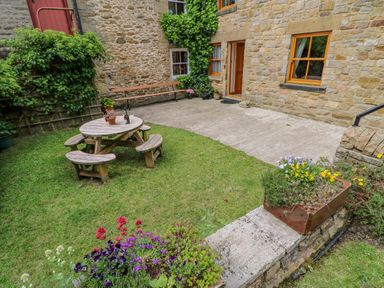An outdoor garden area with a wooden picnic table and benches flowers and plants around the grass at Moorgair Cottage in Slaley near Hexham