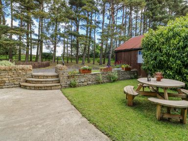 A garden with a wooden picnic table a stone wall with flower pots and trees at Moorgair Cottage in Slaley near Hexham