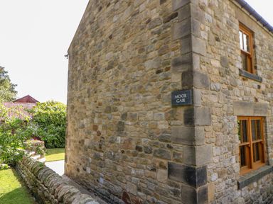 The exterior corner of a stone building with windows and a sign reading Moor Gair near a garden at Moorgair Cottage in Slaley near Hexham