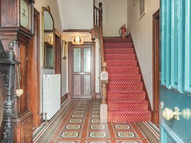 An entrance hallway with a wooden staircase carpeted in red and patterned tile floor at Pensarn Hall in Llanbedr near Harlech