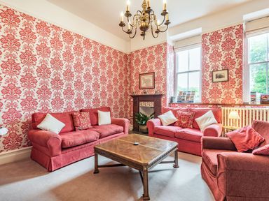 A sitting room with red patterned wallpaper red sofas armchair wooden coffee table and chandelier at Pensarn Hall in Llanbedr near Harlech
