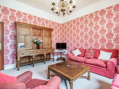 A sitting room with red patterned wallpaper wooden cabinet red sofas and a wooden coffee table at Pensarn Hall Llanbedr near Harlech