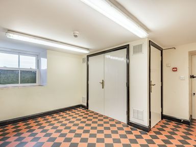 A room with checkered floor tiles two white doors and a window at Pensarn Hall in Llanbedr near Harlech