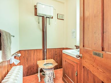 A small toilet with a high cistern toilet and a wooden sink cabinet at Pensarn Hall in Llanbedr near Harlech