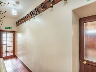 A hallway with a tiled floor wooden doors a row of wall hooks and a row of horse brasses with bells at Pensarn Hall Llanbedr near Harlech