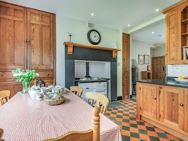 A kitchen with wooden cabinets a table set with teapots cups and flowers at Pensarn Hall in Llanbedr near Harlech