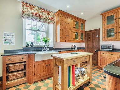 A kitchen with wooden cabinets a kitchen island a window with floral blinds and a patterned floor at Pensarn Hall in Llanbedr near Harlech