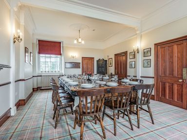 A dining room with a long wooden table set with plates and glasses surrounded by wooden chairs at Pensarn Hall in Llanbedr near Harlech