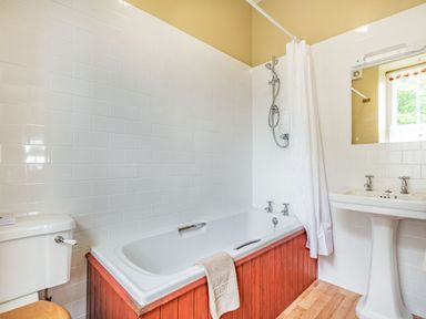 A bathroom with a bathtub, showerhead, sink with two taps, mirror, toilet, and white tiled walls at Pensarn Hall in Llanbedr near Harlech