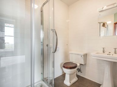 A bathroom with a shower cubicle toilet with a dark seat and a pedestal sink at Pensarn Hall in Llanbedr near Harlech