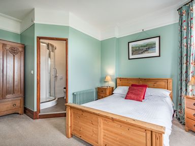 A bedroom with a wooden bed and bedside tables with lamps a wooden wardrobe and an ensuite bathroom at Pensarn Hall in Llanbedr near Harlech