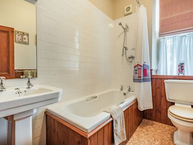 A bathroom with a bathtub shower sink toilet and window with curtain at Pensarn Hall in Llanbedr near Harlech
