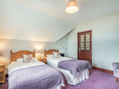 A bedroom with two single beds a wooden door with stained glass and a small fireplace at Pensarn Hall in Llanbedr near Harlech