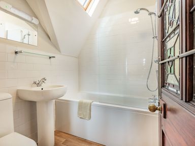A bathroom with a bathtub shower combination a pedestal sink a toilet and a stained glass door at Pensarn Hall in Llanbedr near Harlech