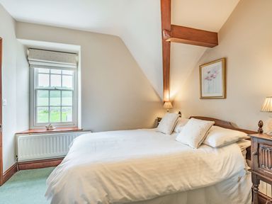 A bedroom with a bed with white bedding two pillows bedside tables with lamps a window and a framed picture on the wall at Pensarn Hall in Llanbedr near Harlech