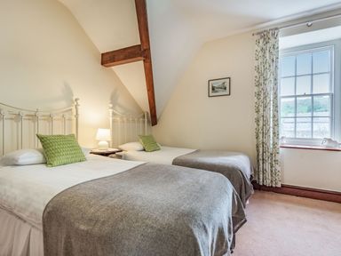 A bedroom with two single beds a bedside table with lamp a window and a framed picture on the wall at Pensarn Hall in Llanbedr near Harlech