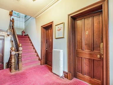 A hallway with red carpeted stairs and two wooden numbered doors with a white radiator and framed picture at Pensarn Hall Llanbedr near Harlech