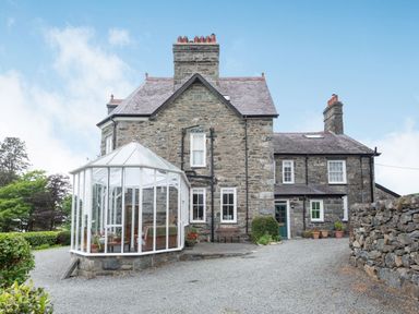 An exterior view of a stone house with a glass conservatory and gravel driveway at Pensarn Hall in Llanbedr near Harlech