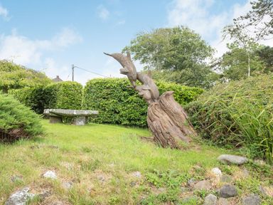 A garden with a stone bench and a wooden dolphin sculpture surrounded by grass and bushes at Pensarn Hall in Llanbedr near Harlech