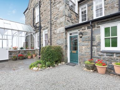 Stone exterior of a house with a green door and potted plants on a gravel area at Pensarn Hall in Llanbedr near Harlech