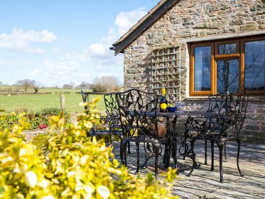 An outdoor seating area with a metal table and chairs on a stone patio beside a stone house at Stargazer's Field House in Hardwicke near Hay-on-Wye