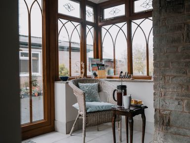 A corner with a wicker chair and cushions next to a small wooden table with a coffee press, cup, and plate of pastries at Stargazer's Field House in Hardwicke near Hay-on-Wye