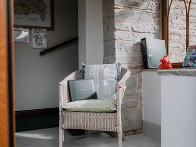 A wicker chair with cushions and a visitors book in a room with a stone wall and window at Stargazer's Field House in Hardwicke near Hay-on-Wye