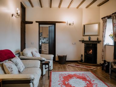 A living room with cream sofas floral cushions a wood burning stove and rugs at Stargazer's Field House Hardwicke near Hay-on-Wye