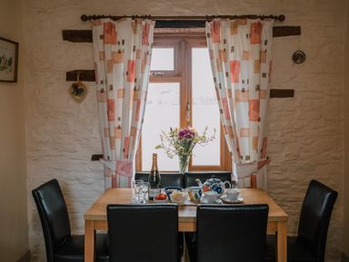A dining table with black chairs by a window with curtains and flowers on the table at Stargazer's Field House in Hardwicke near Hay-on-Wye