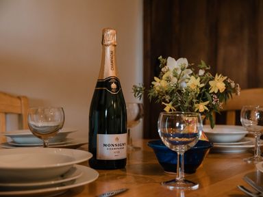A dining table set with plates wine glasses a bottle of champagne and a flower arrangement at Stargazer's Field House in Hardwicke near Hay-on-Wye