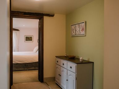 A hallway with a white sideboard and framed artwork next to a bedroom with a bed and a painting on the wall at Stargazer's Field House in Hardwicke near Hay-on-Wye