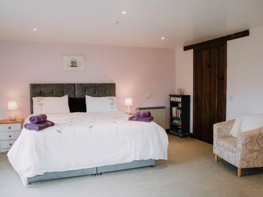 A bedroom with a double bed and two bedside tables with lamps a bookshelf a wooden door and an armchair at Stargazer's Field House in Hardwicke near Hay-on-Wye
