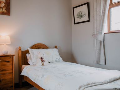 A bedroom with a single wooden bed and floral bedding a bedside table with a lamp and a window with curtains at Stargazer's Field House Hardwicke near Hay-on-Wye