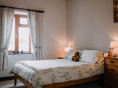 A bedroom with a bed with floral bedding a teddy bear on it two bedside tables with lamps and a window with curtains at Stargazer's Field House in Hardwicke near Hay-on-Wye