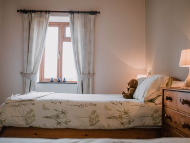 A bedroom with a bed with floral bedding a teddy bear on the bed wooden dresser and a window with curtains at Stargazer's Field House Hardwicke near Hay-on-Wye