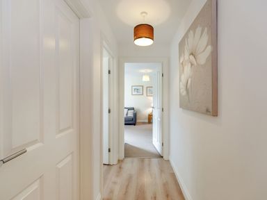A hallway with wooden floor lamps and flower artwork leading to a living room with a sofa at Perriwinkle The Bay near Filey